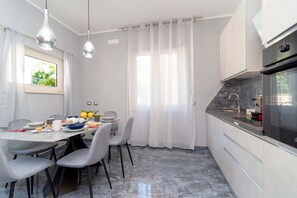 Eine moderne Küche mit Essbereich, ausgestattet mit einer Marmorarbeitsplatte, einem eingebauten Backofen und einem Esstisch mit Stühlen.