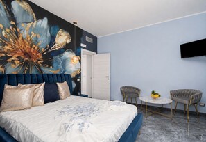 Ein Schlafzimmer mit einem großen Bett, einem an der Wand montierten Fernseher, zwei Stühlen und einem kleinen Tisch mit Obst.