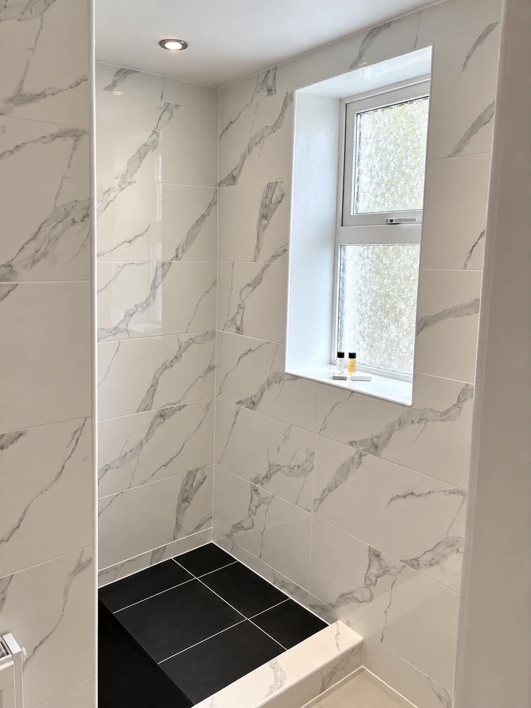 A bathroom with marble tiles, a window with a view, and a black sink.