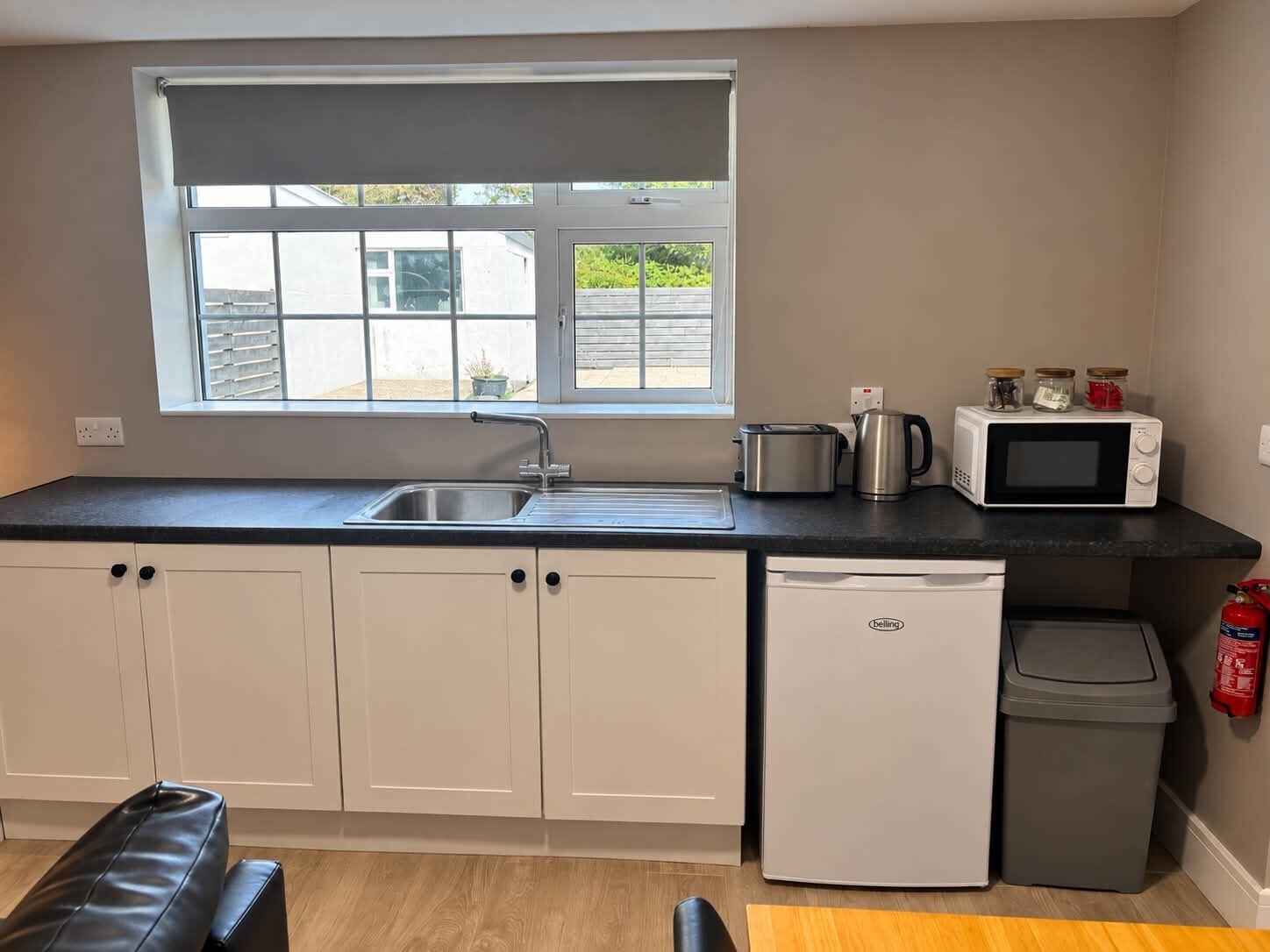 Eine kleine Küche mit Fenster, Spüle, Mikrowelle, Toaster und Kühlschrank.