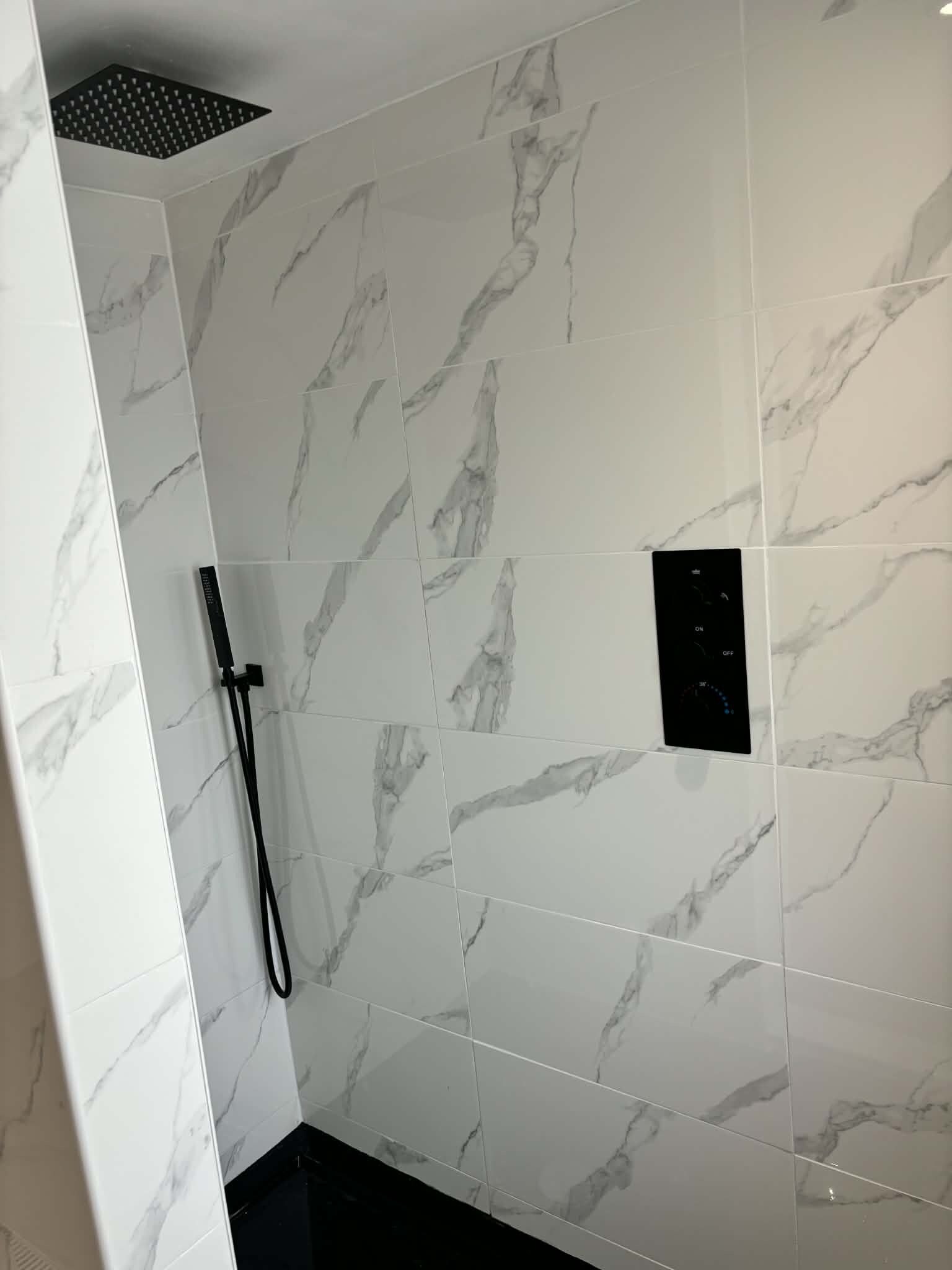 Une salle de bain avec des carreaux de marbre blanc, une pomme de douche et un panneau de commande.
