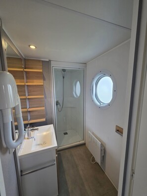 A modern bathroom with a glass-enclosed shower, a white sink, and a small window. - 5-Star Houlgate Campground - 2-bedroom, 4-person mobile home with AC, facing the pool. 1.5 km from the beach (houlgate)