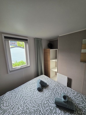 Quarto de hotel com cama, janela com cortinas, ventilador e estante embutida.