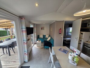 Um espaço compacto com sofá, mesa de jantar, televisão e pequeno espaço de cozinha.