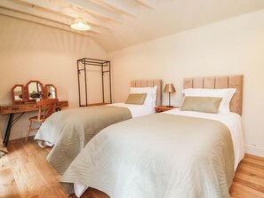 A bedroom with two beds, a desk with a mirror, and a hanging light fixture. - Lyneal Cottage (Ellesmere)