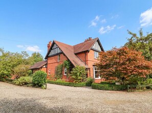 A two-story house with a steeply pitched roof, brick walls, and a gravel driveway. - Lyneal Cottage (Ellesmere)