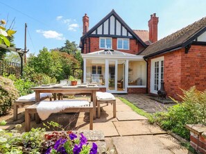 A traditional house with a conservatory, a patio with a table and chairs, and a garden with various plants. - Lyneal Cottage (Ellesmere)
