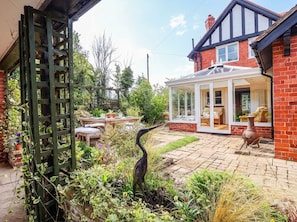 A garden with a conservatory, a brick house, and a bird sculpture. - Lyneal Cottage (Ellesmere)