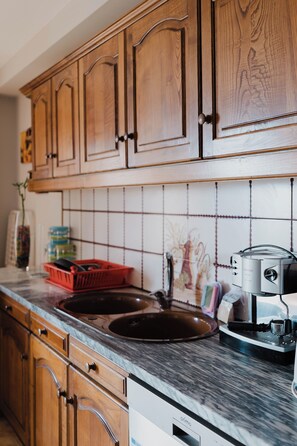 A kitchen with wooden cabinets, a tiled backsplash, a sink, a coffee machine, and a red basket.