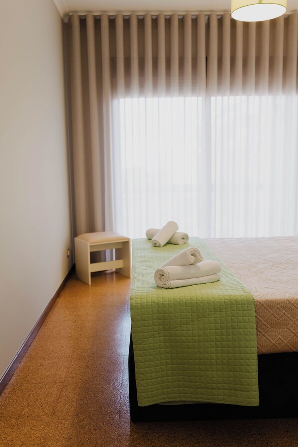 A hotel room with a bed, a small bedside table, and a window with curtains.