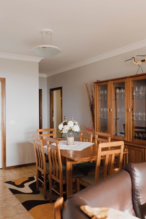A dining area with a wooden table, chairs, a vase with flowers, a cabinet with glass doors, and a ceiling light fixture.