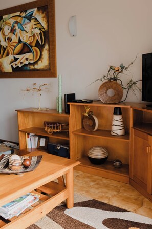 A living room with a wooden coffee table, a bookshelf, a television, and a painting on the wall.