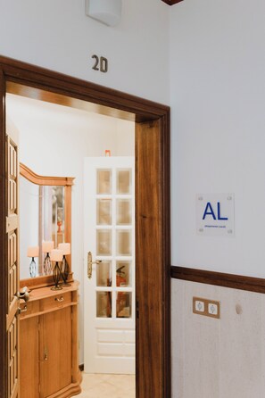 Entrada d'una habitació d'hotel amb una porta de fusta, un mirall, un taulell i un senyal de paret que diu 'AL' per 'Alojamento Local'.