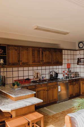 A kitchen with wooden cabinets, a marble countertop, and a stainless steel refrigerator.