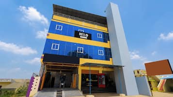 A multi-story hotel with a blue and yellow facade, a visible entrance with steps, and a sign indicating it is serviced by OYO.