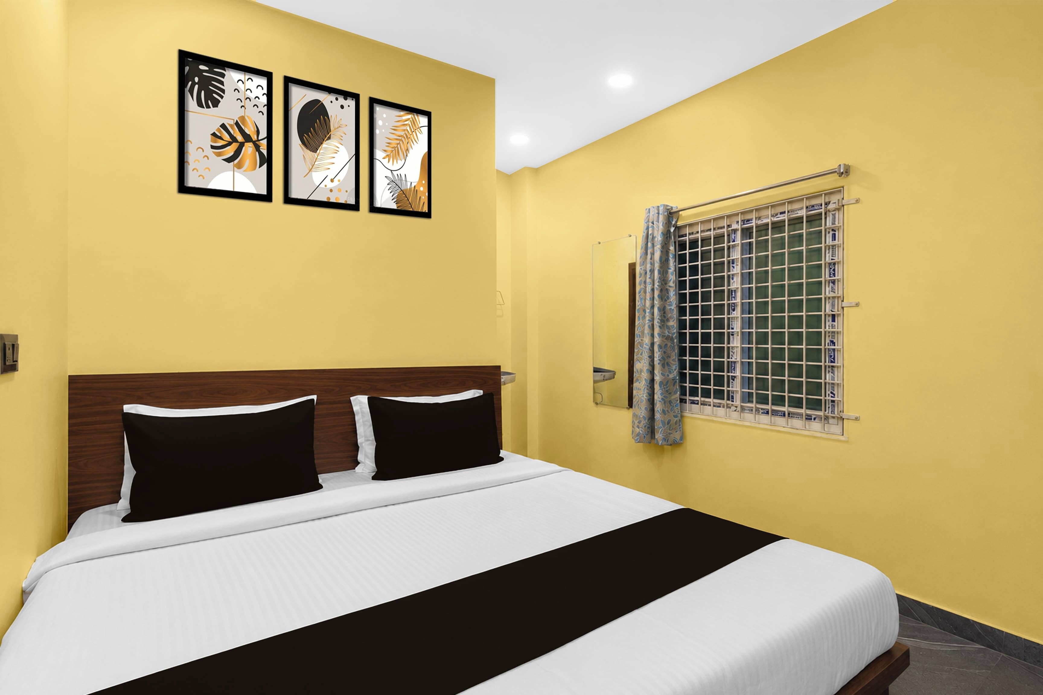 Una habitación de hotel con una cama, un ventanal con reja de metal y tres cuadros enmarcados en la pared.