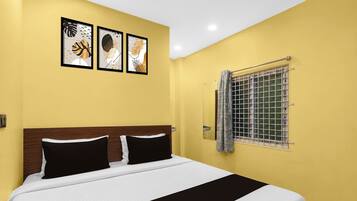 Una habitación de hotel con una cama, un ventanal con reja de metal y tres cuadros enmarcados en la pared.