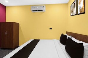 A hotel room with a bed, a wardrobe, an air conditioning unit, and wall art.