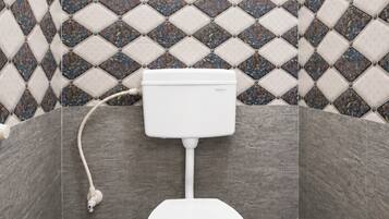 A bathroom with a toilet, a wall-mounted sink, and a patterned tile backsplash.