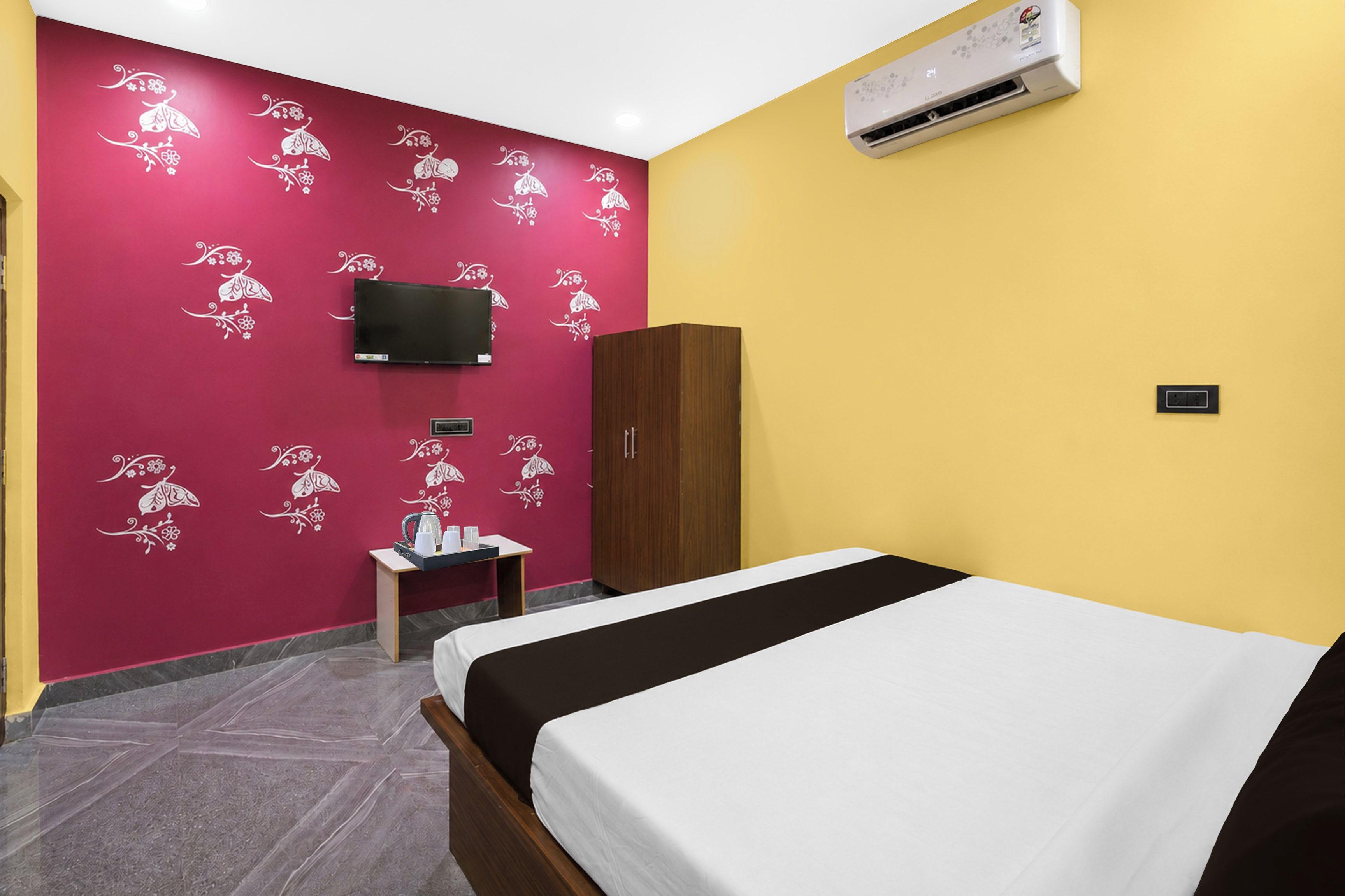 Een hotelkamer met een bed, een aan de muur bevestigde televisie, een kledingkast, een klein tafeltje met een waterkoker en een airconditioning.