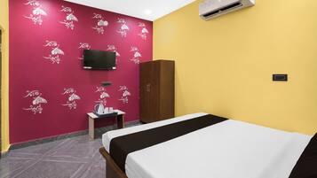Een hotelkamer met een bed, een aan de muur bevestigde televisie, een kledingkast, een klein tafeltje met een waterkoker en een airconditioning.