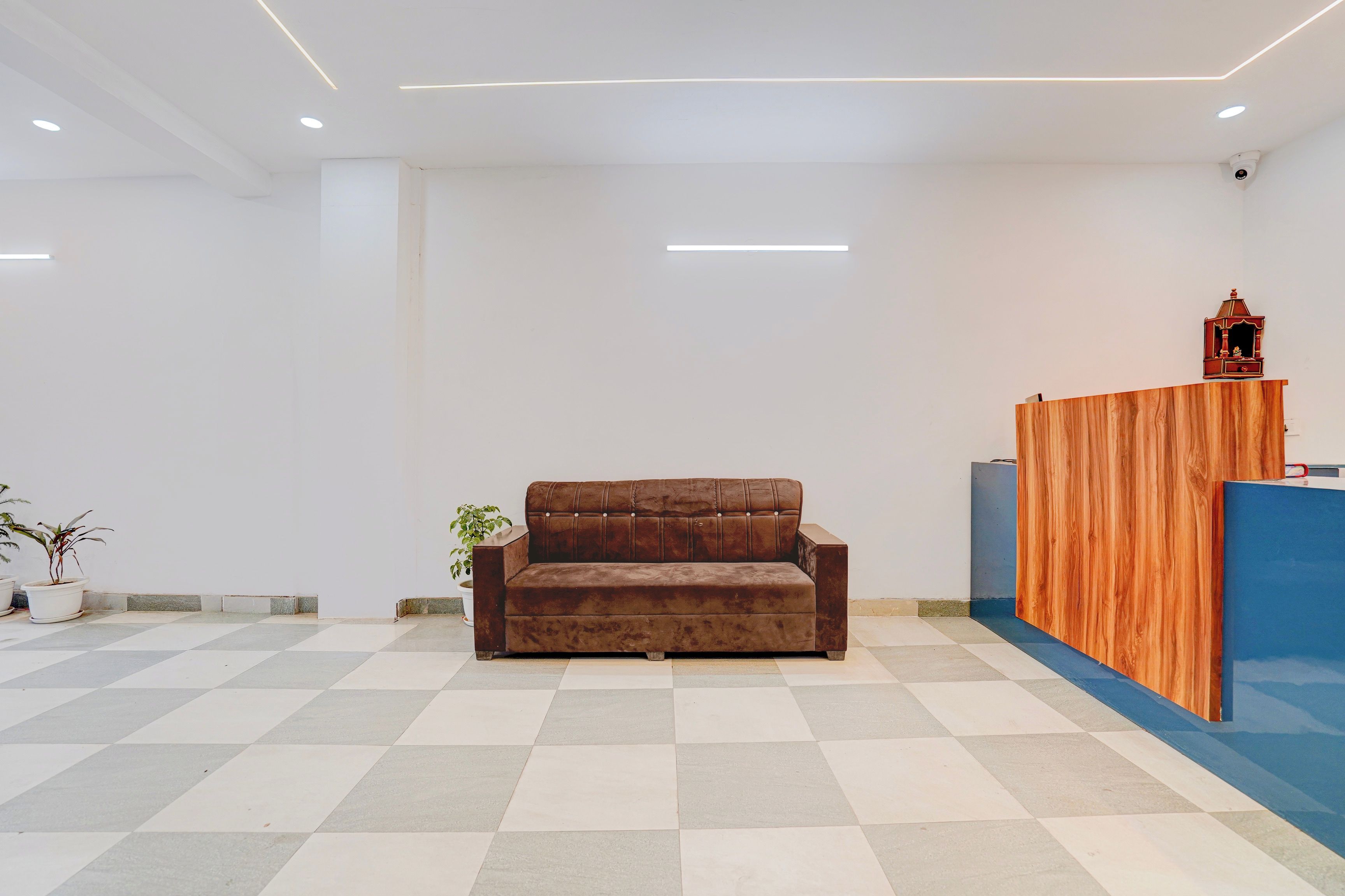 A reception area with a brown sofa, a wooden reception desk, and potted plants.