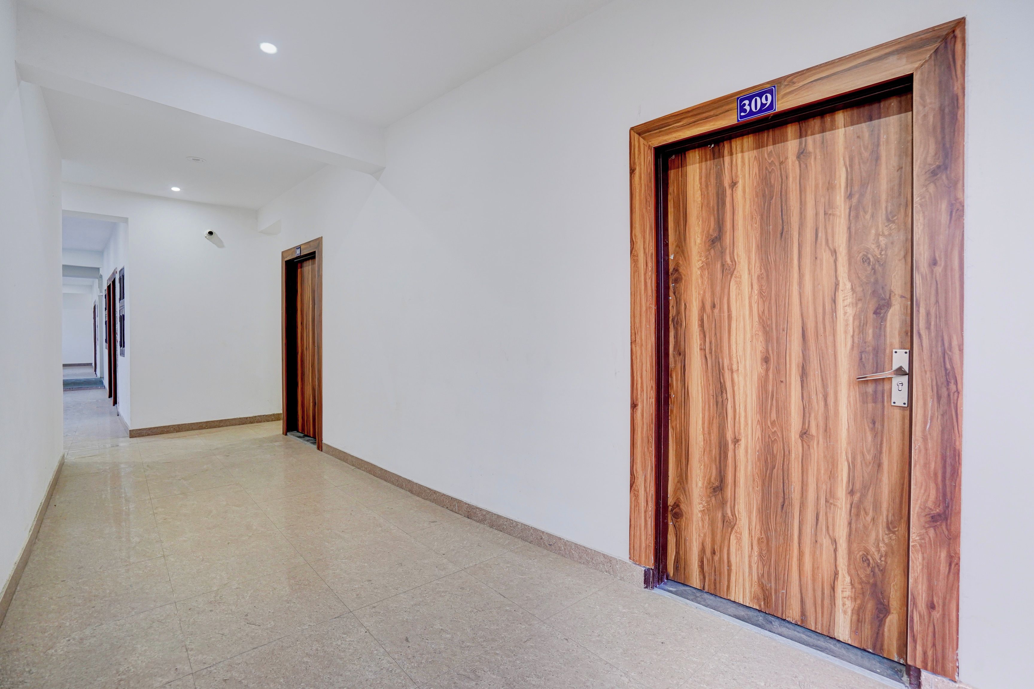 Un pasillo con una puerta de madera marcada con el número '309' y una cámara en la pared.