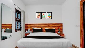 A hotel room with a bed, a wooden headboard, a mirror, and three framed artworks on the wall.