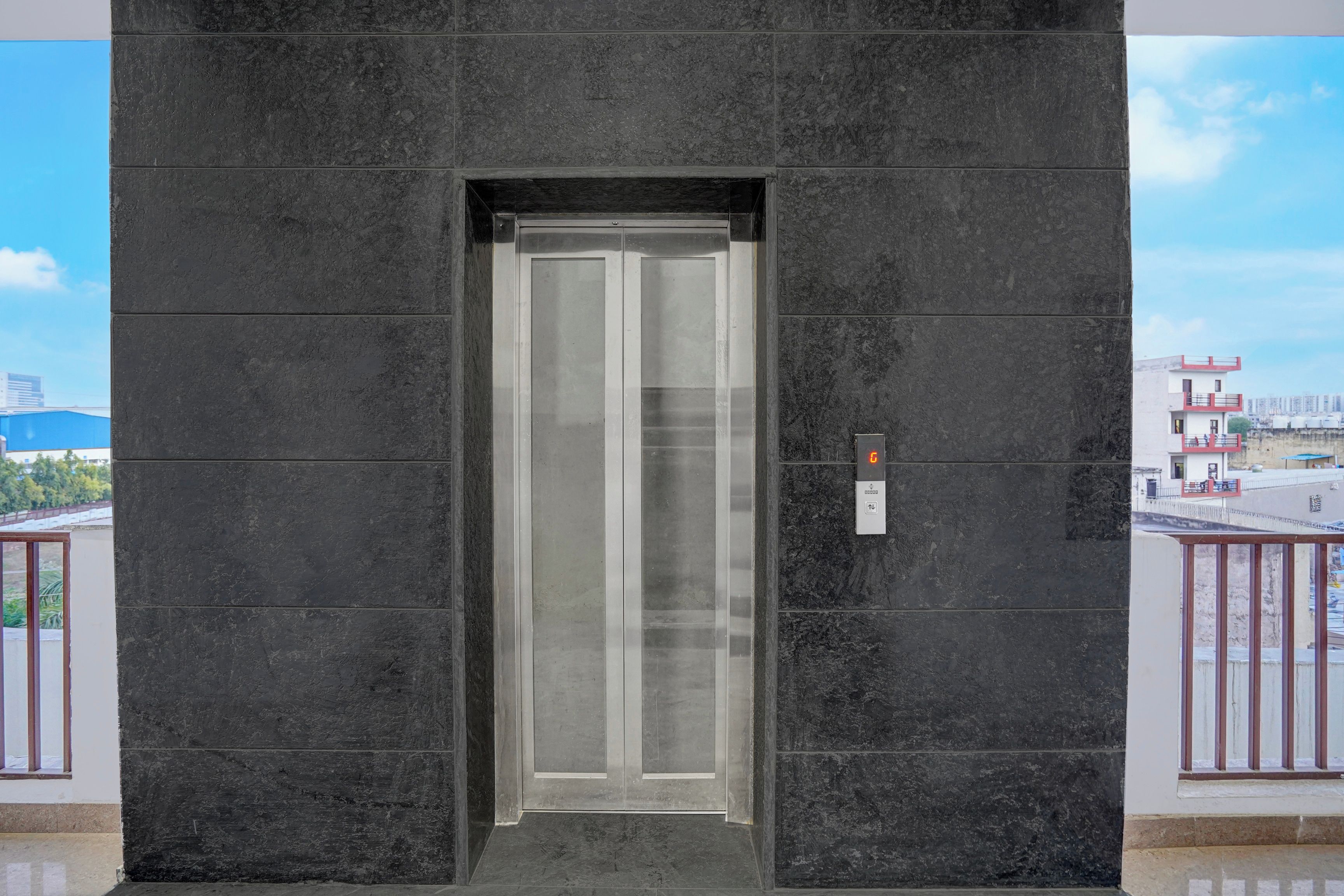 A modern elevator with a metallic finish, set within a building with dark stone walls.