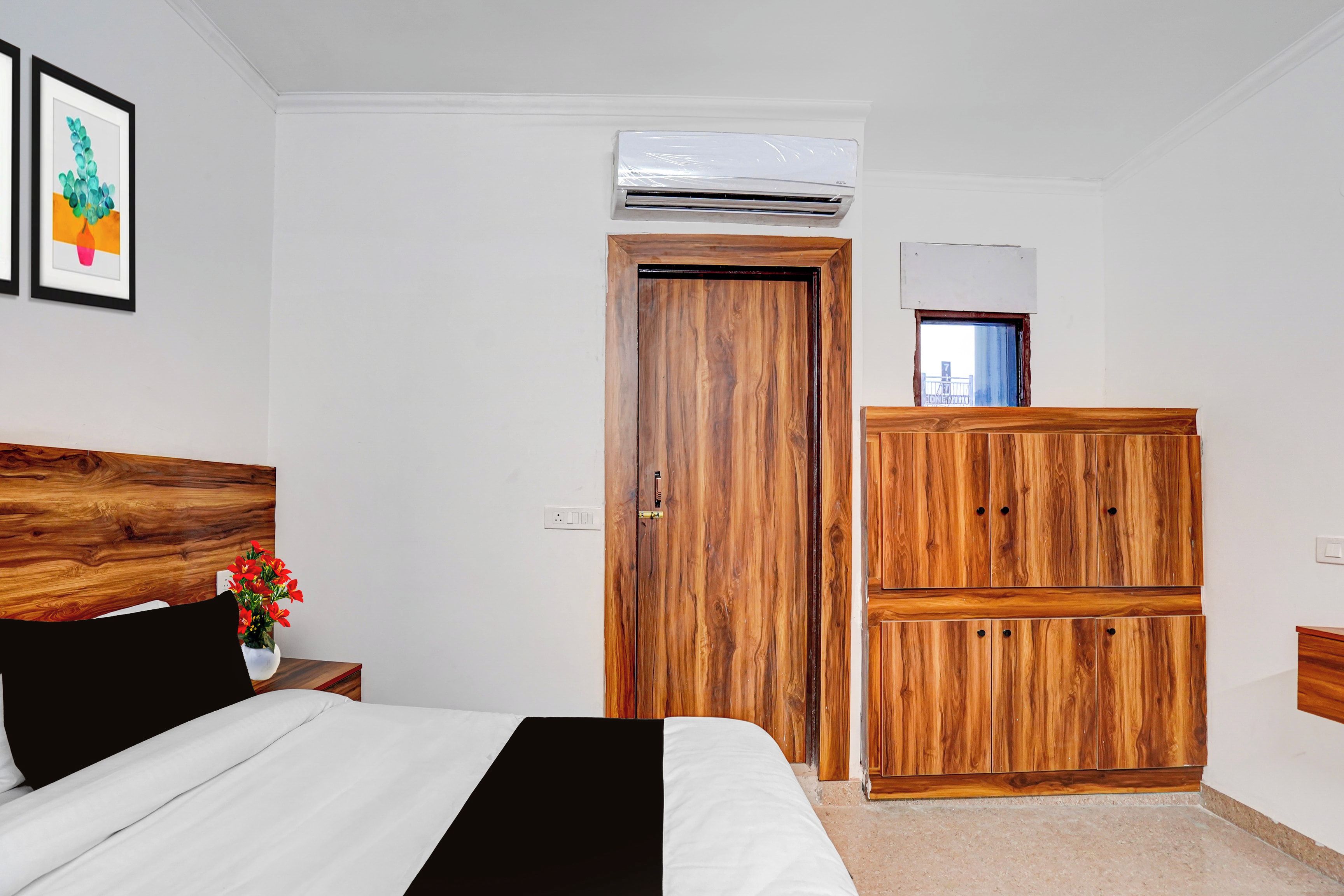 Un dormitorio con cama, armario de madera, equipo de aire acondicionado y una ventana pequeña.