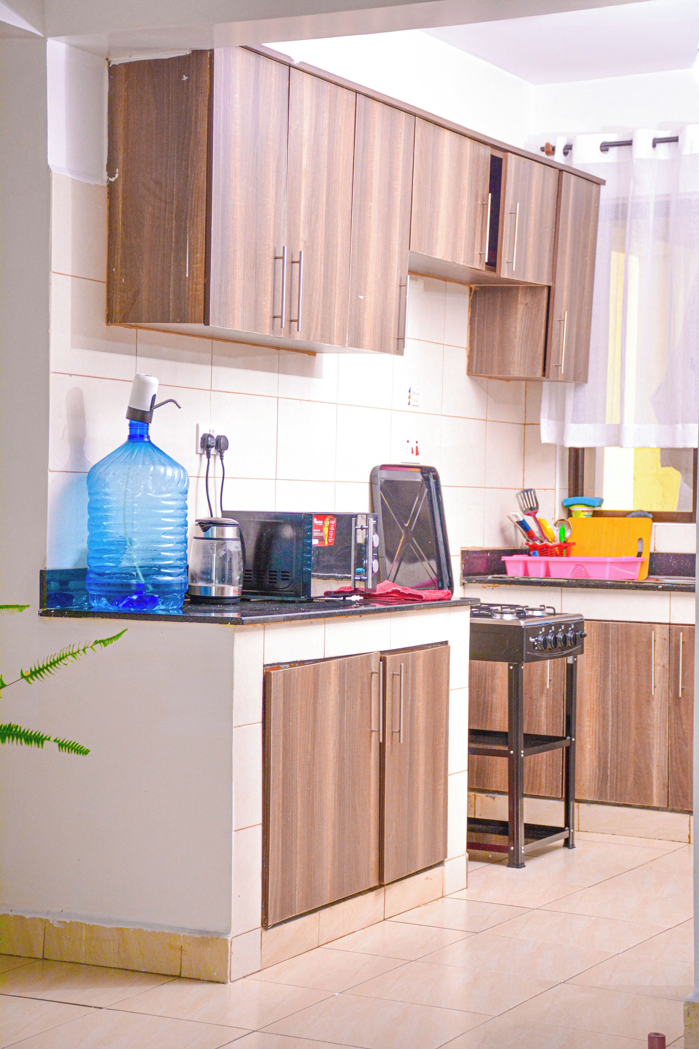 Una cocina con gabinetes de madera, un dispensador de agua grande, una cafetera, un tostador y una estufa a gas.
