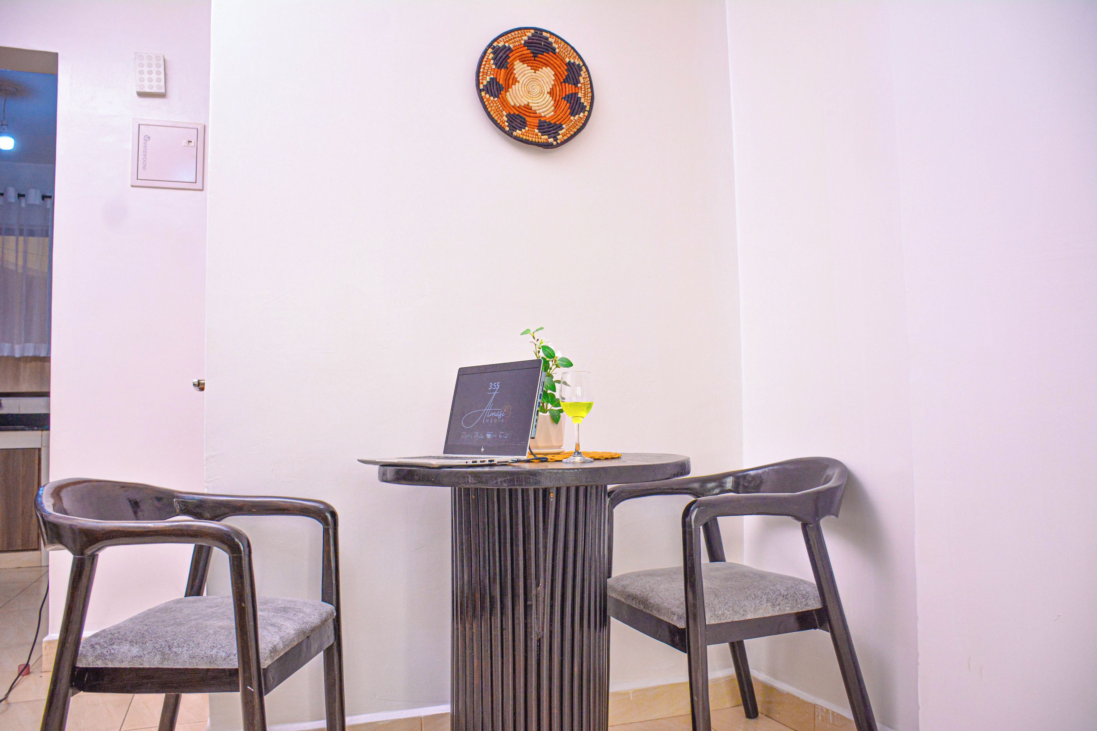 Una habitación con dos sillas, una mesita con una computadora portátil, una planta en maceta y un plato decorativo en la pared.
