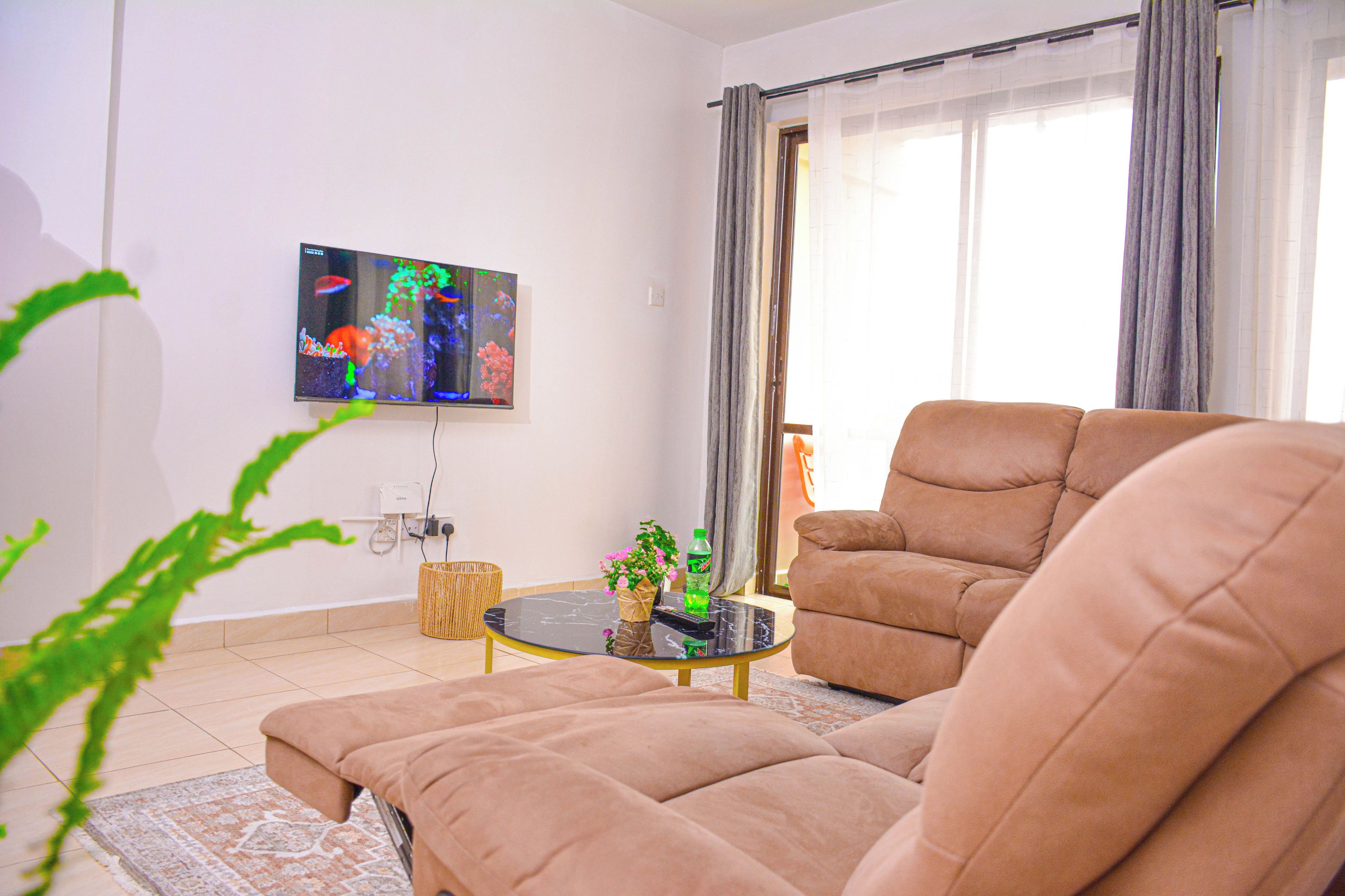 Un salon comprenant un canapé, une table basse, un téléviseur fixé au mur et une fenêtre avec des rideaux.