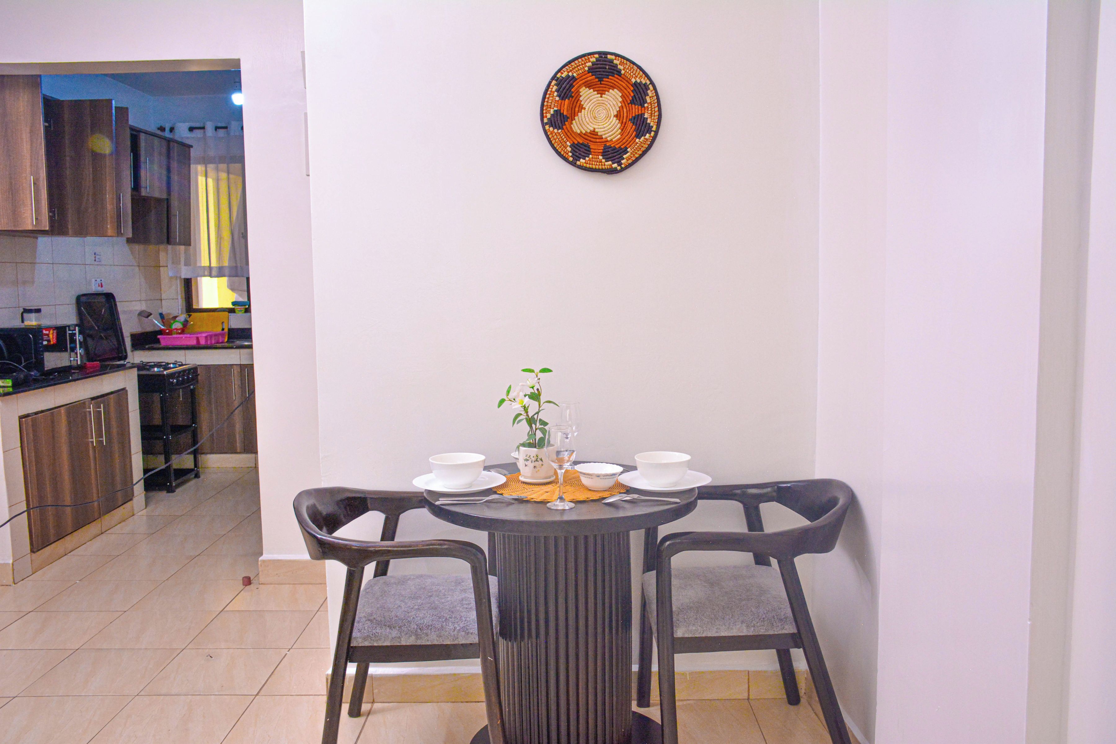 Un coin repas comprenant une table ronde, deux chaises, un vase avec des fleurs et une assiette décorative fixée au mur.