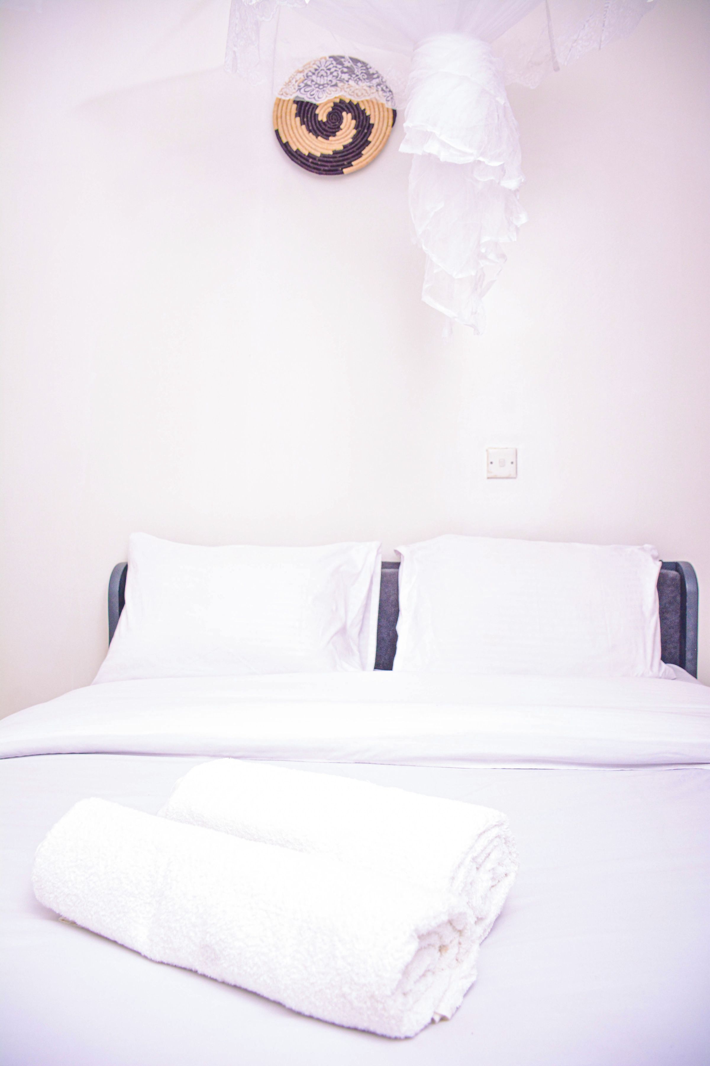 Una cama con ropa blanca, una toalla blanca doblada y un adorno en la pared.