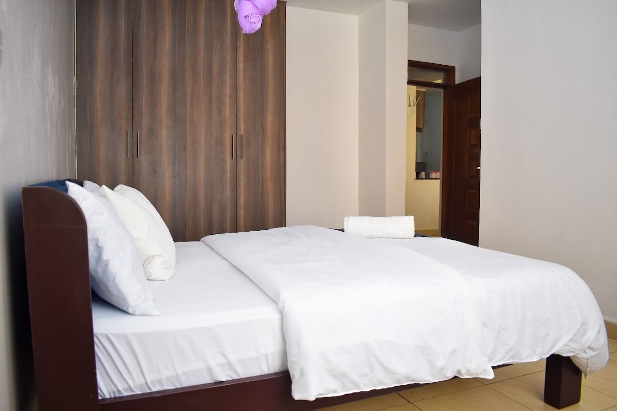 A neatly made bed with white linens and a wooden headboard in a hotel room.