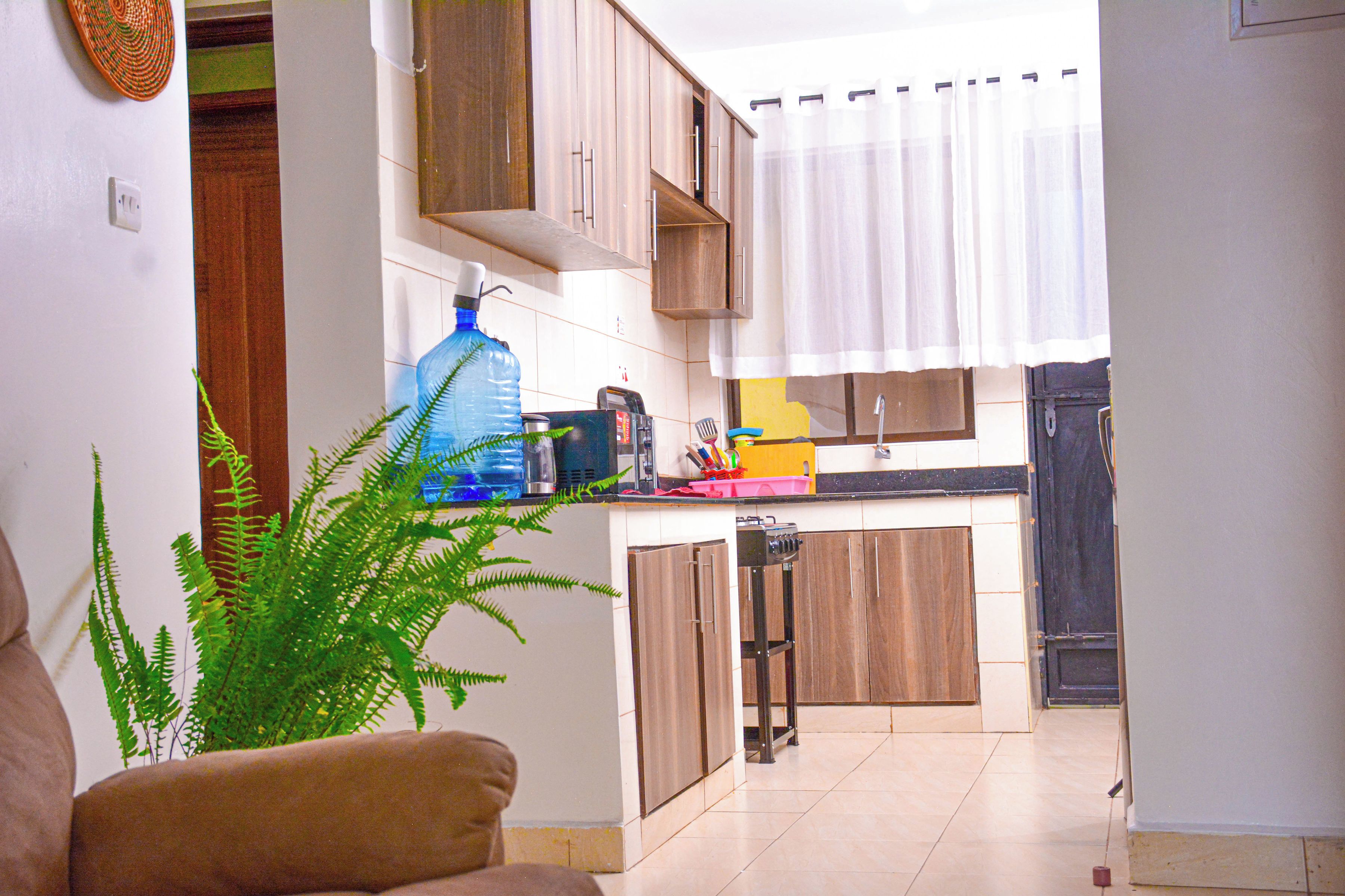Una cocina compacta con armarios de madera, un dispensador de agua grande y un comedor con sofá.