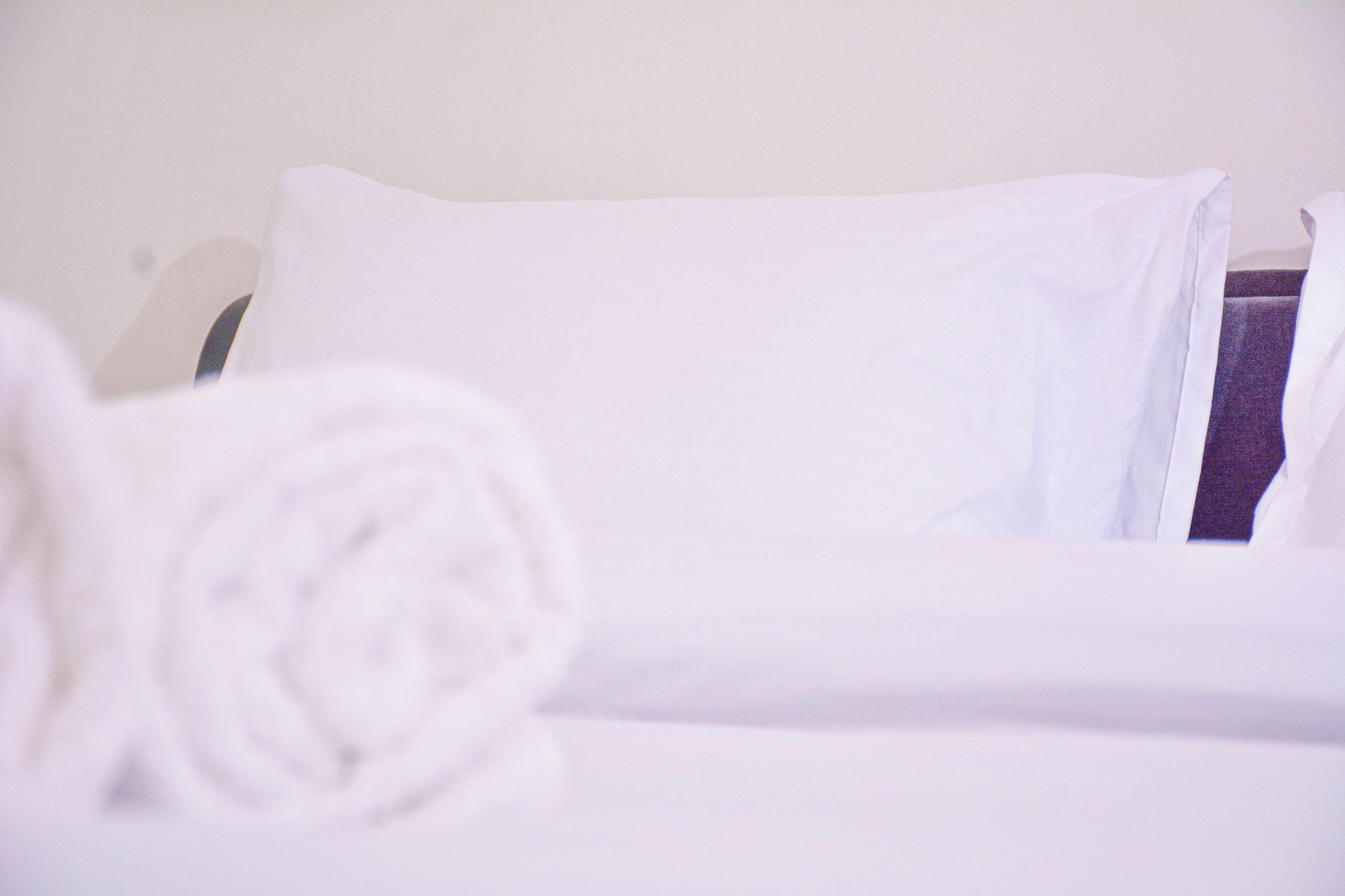 Una cama bien hecha con sábanas blancas y una toalla enrollada.