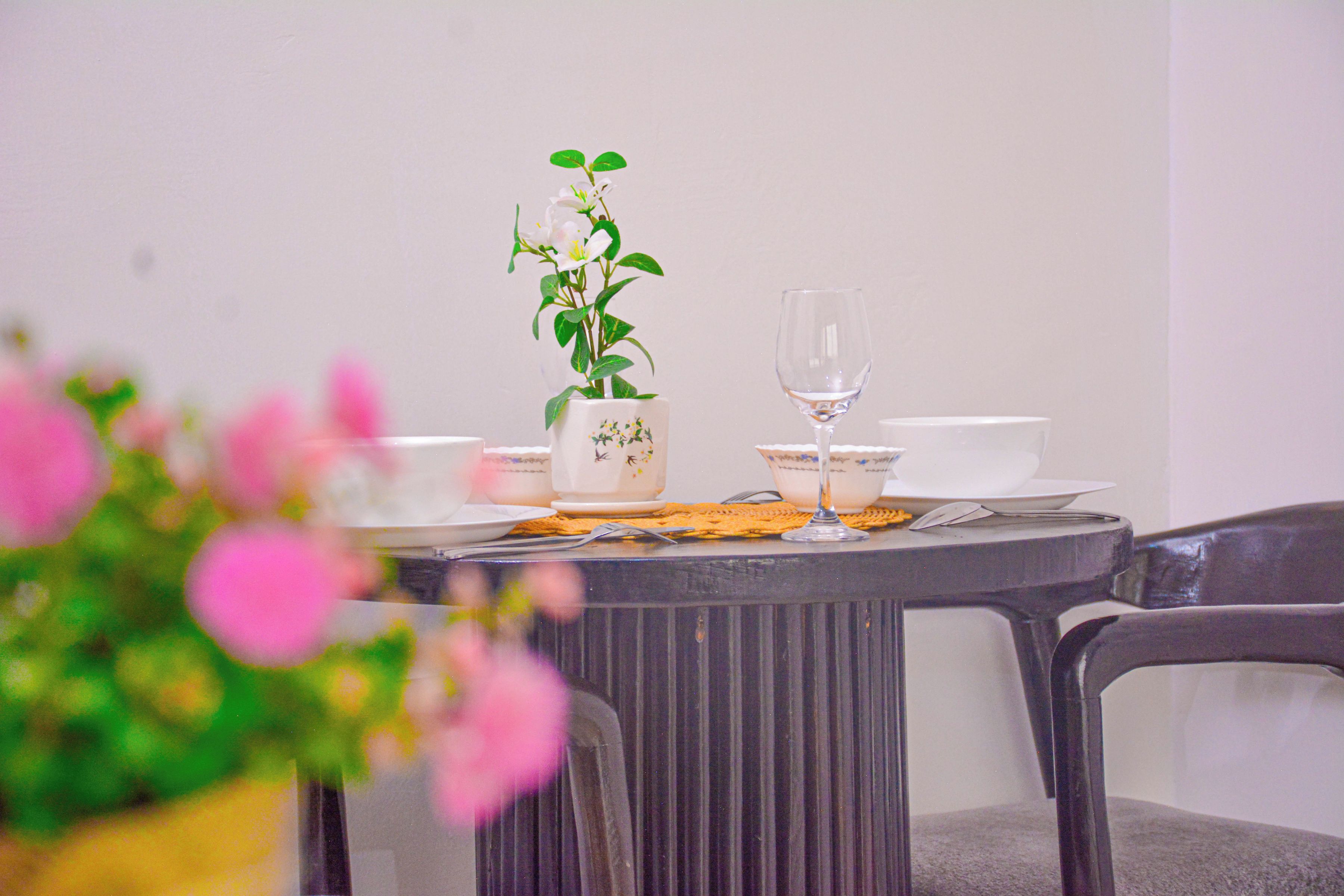 Una mesa de comedor dispuesta con platos blancos, una copa y una jarra con estampado floral.