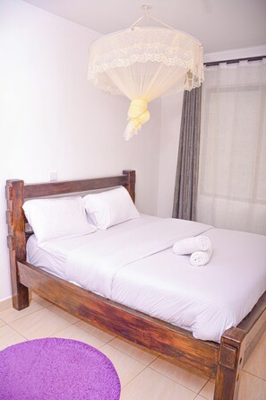 A single bed with a wooden frame and white bedding, a purple rug, and a hanging light fixture.