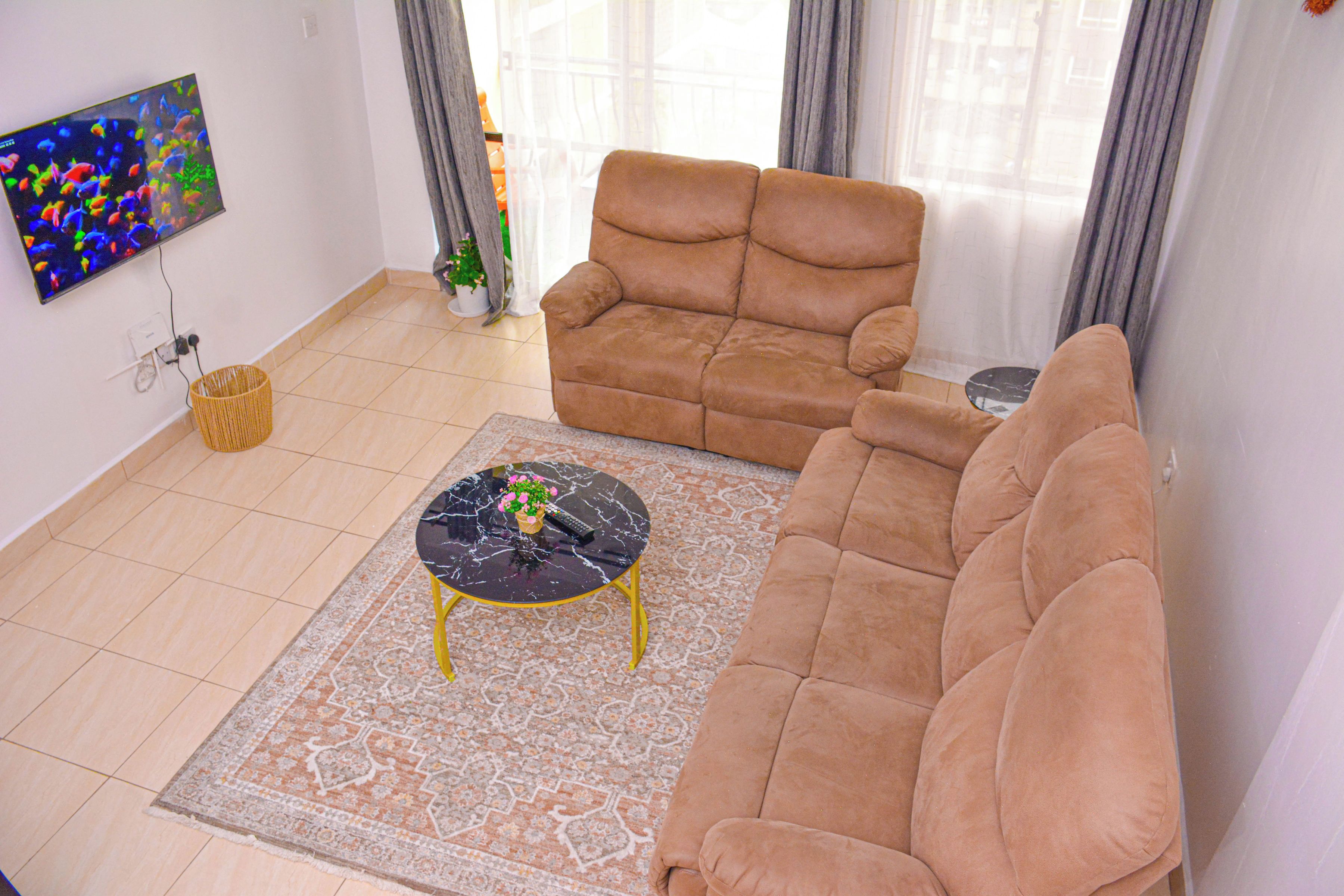 Una sala de estar con un sofá, una mesa de centro con un control remoto, un tapete estampado y un televisor que muestra peces de colores.