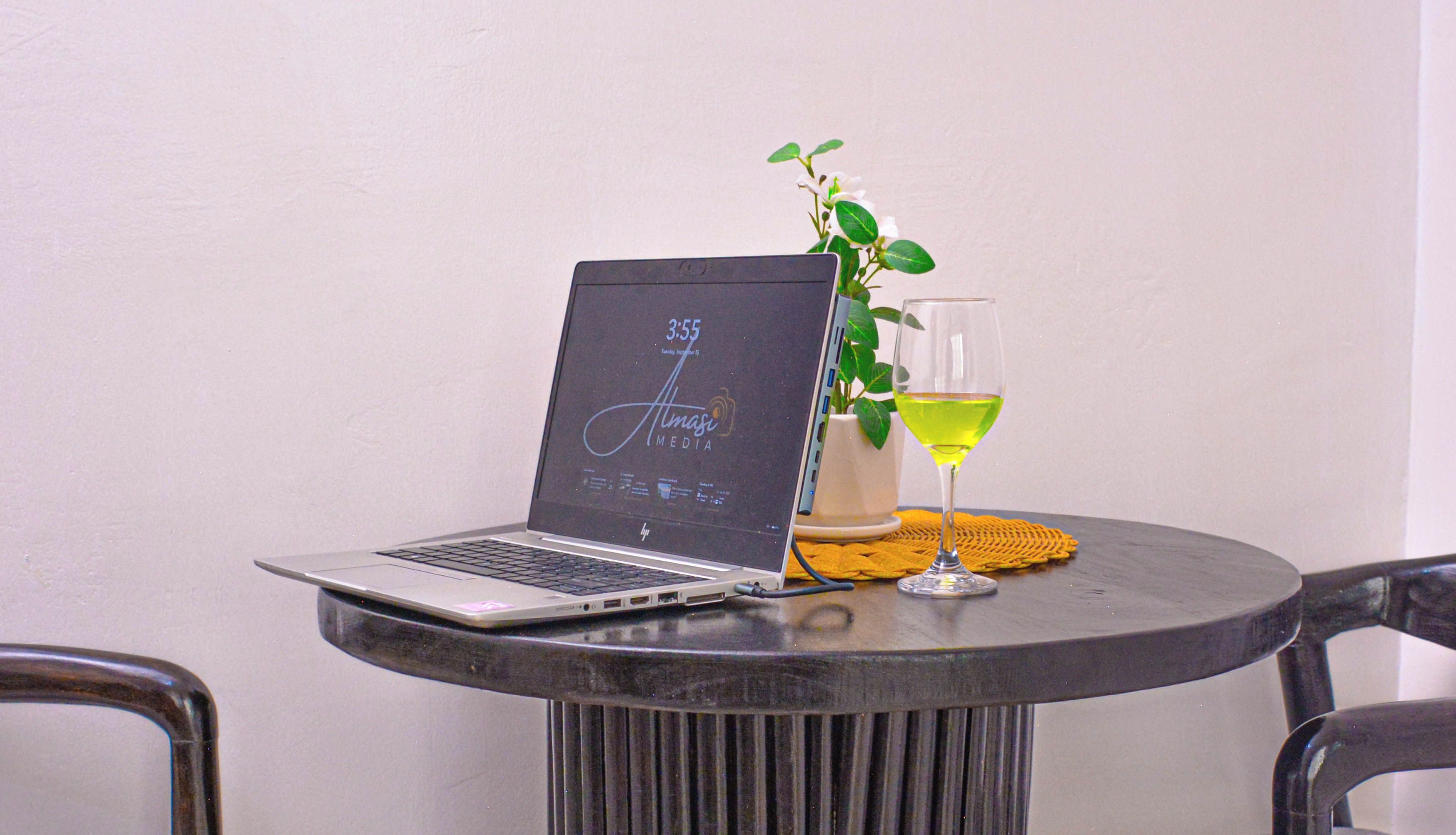 Um laptop sobre uma mesa redonda, com um copo de vinho e um vaso de planta ao lado.