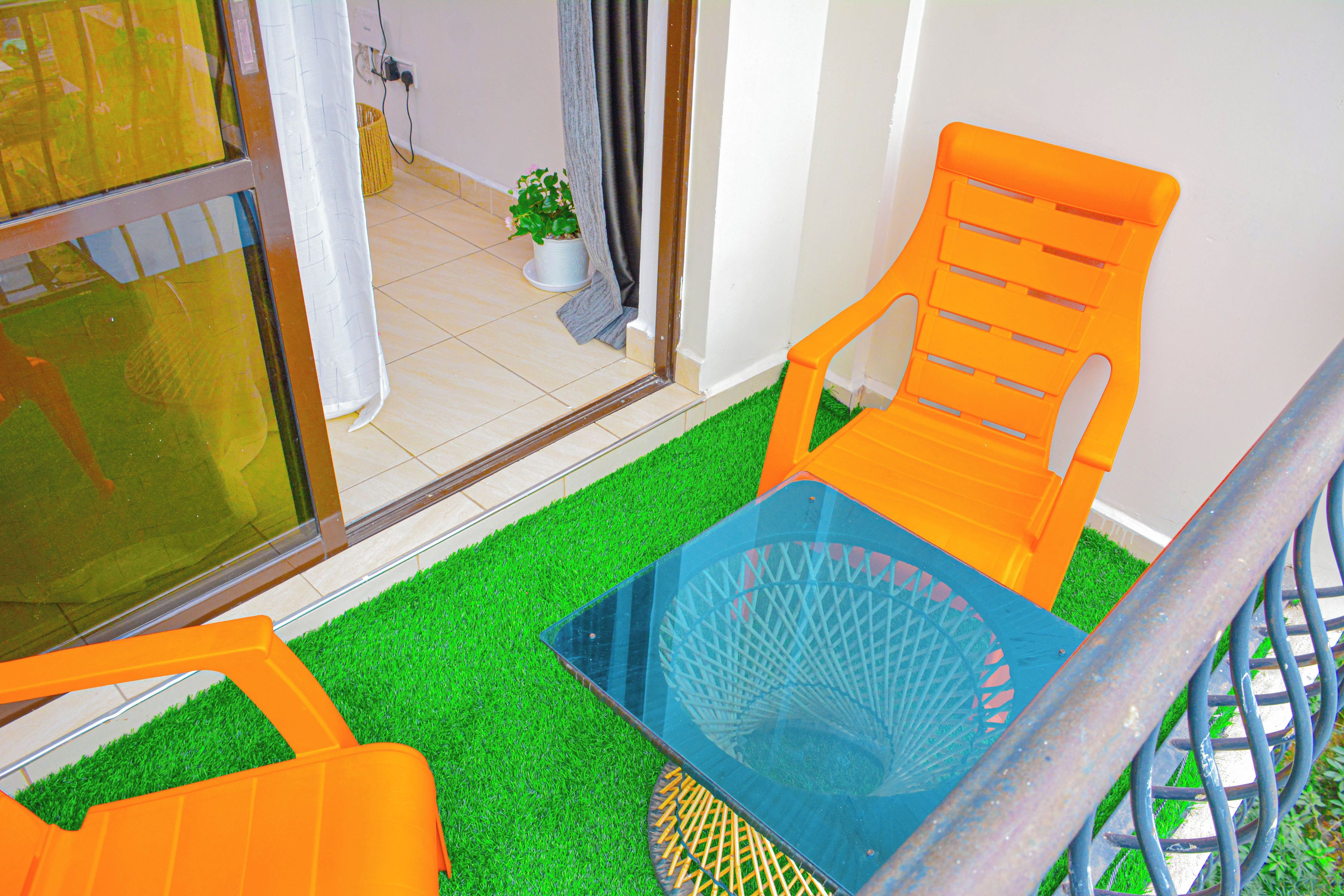 A small outdoor seating area with two orange chairs and a blue table, surrounded by artificial green grass.