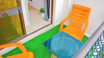 A small outdoor seating area with two orange chairs and a blue table, surrounded by artificial green grass.