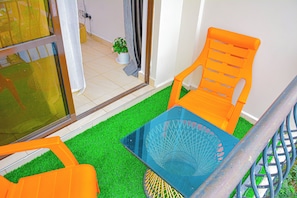A small outdoor seating area with two orange chairs and a blue table, surrounded by artificial green grass.