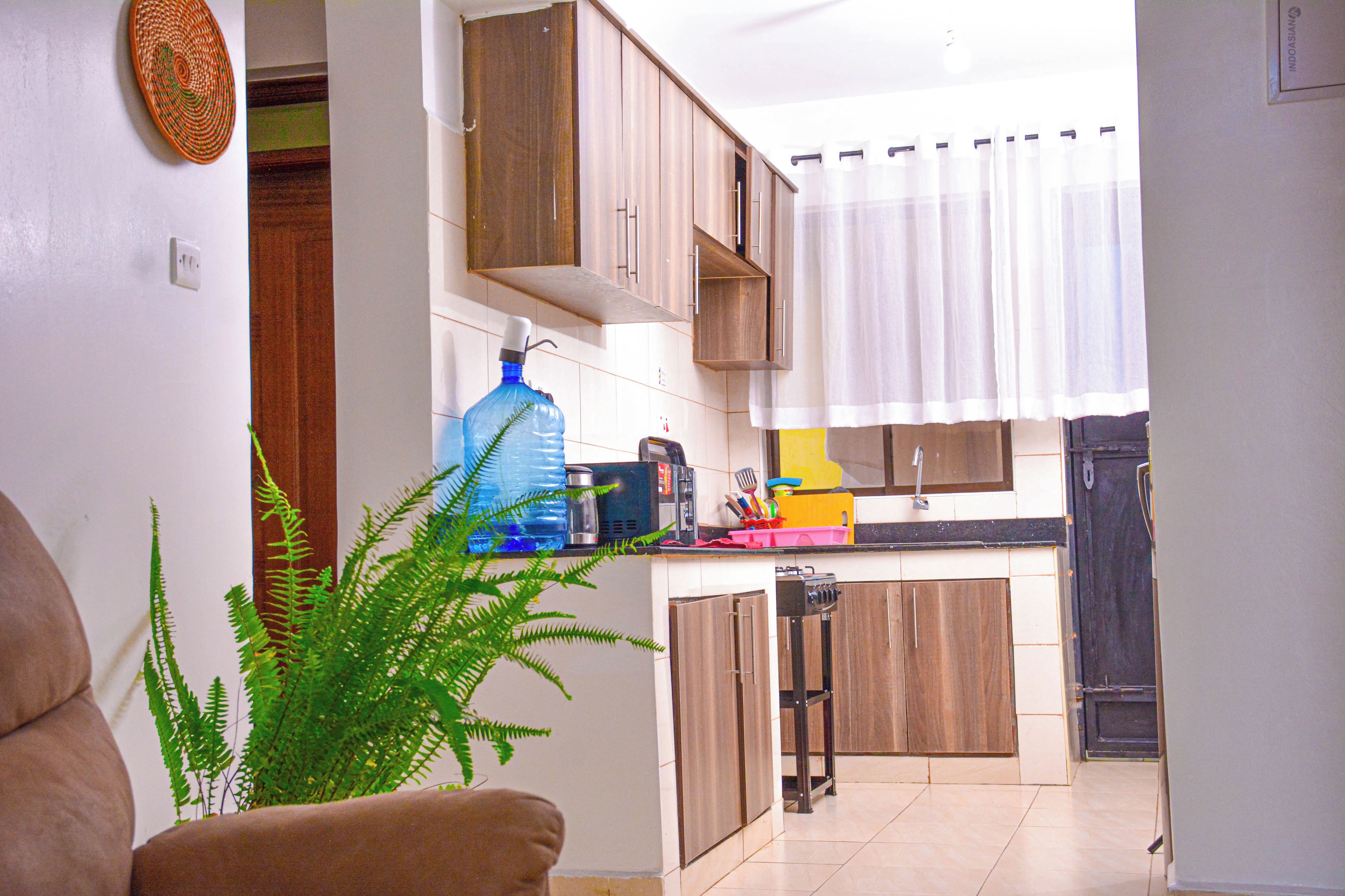 Cocina compacta con muebles de madera, un dispensador de agua grande y un ventanal con cortinas.
