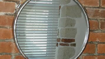 Ein runder Spiegel mit horizontalen Jalousien an einer Ziegelwand.