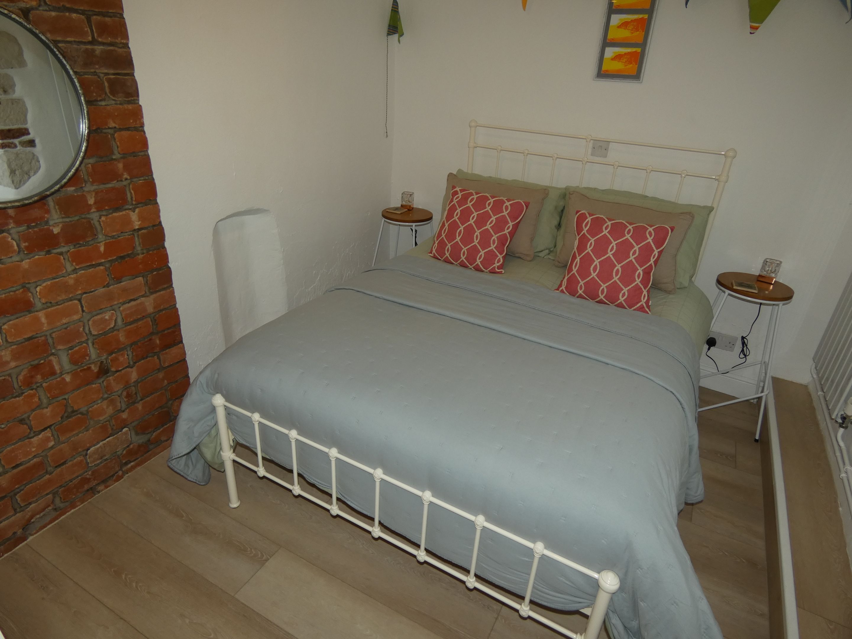 Ein Schlafzimmer mit einem Bett, einer Ziegelwand, einem Heizkörper und einem kleinen Tisch mit einer Lampe.
