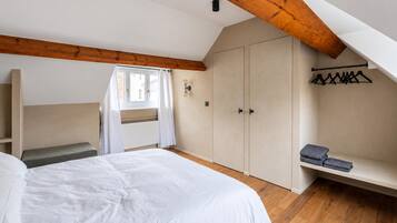 A bedroom with a large bed, a wardrobe, a bench, and a window with curtains.
