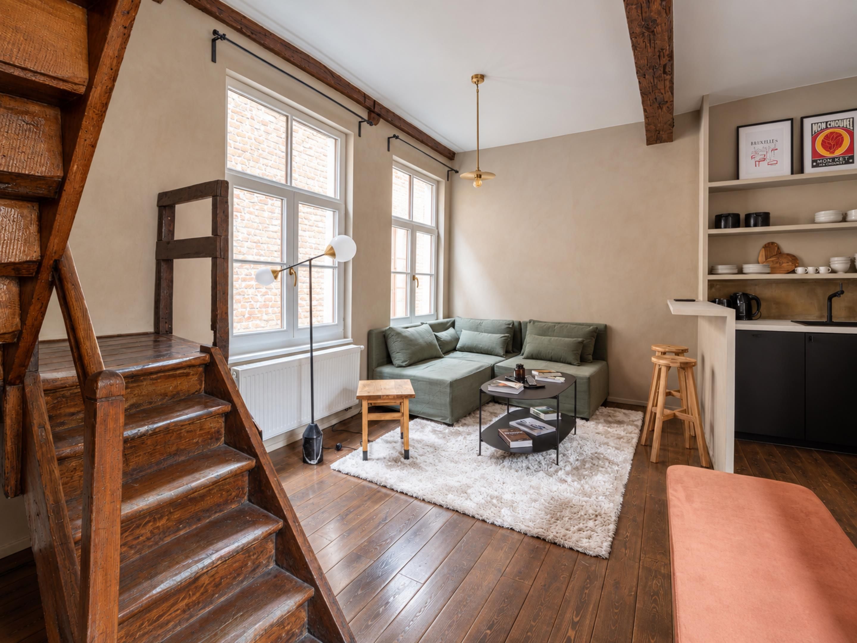 A modern living space with a staircase, a sectional sofa, a coffee table, and a kitchen area with shelves.